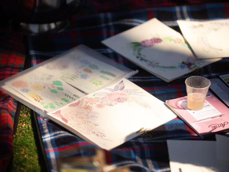 Close up of a variety of watercolour painting materials on a tartan picnic blanket